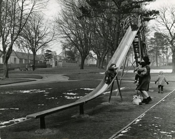 A mother with her children who are playing on a chute in March 1965.