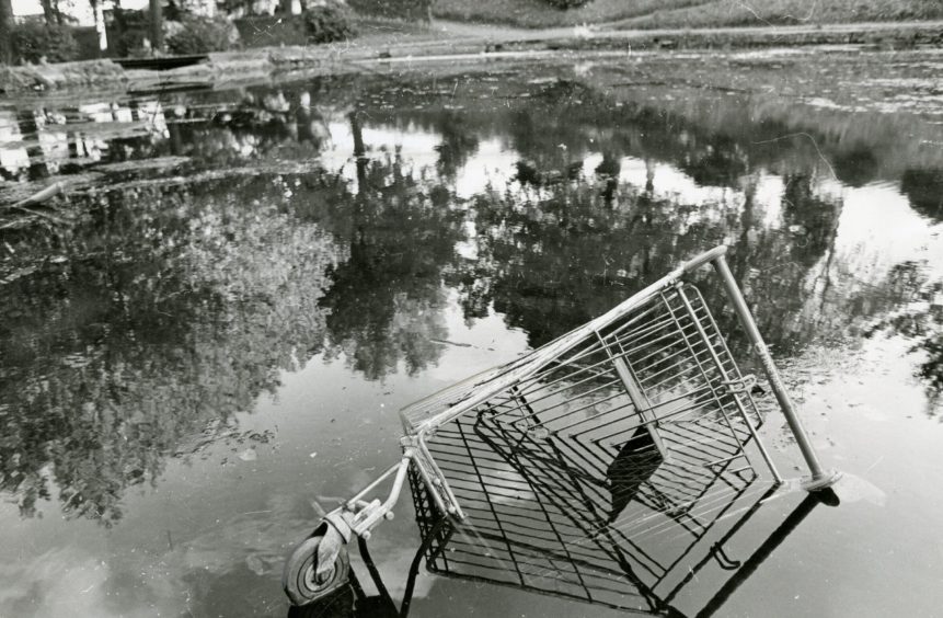 The Den o' Mains pond, filled with rubbish including a shopping trolley.