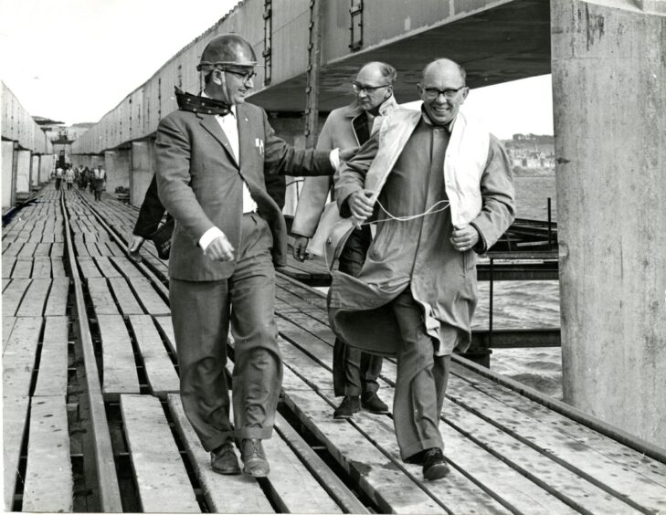 Officials in suits and hardhats walk across the Tay Road Bridge while it is under construction in July 1964. 