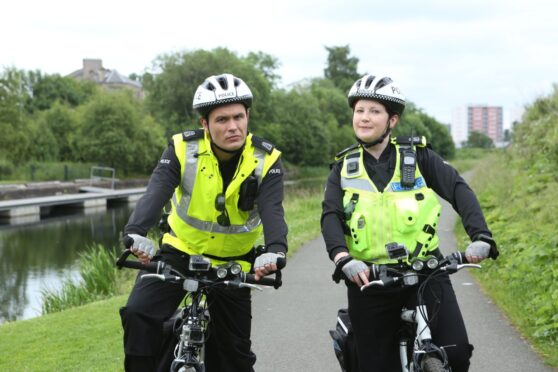 Still from TV comedy show Scot Squad showing actors Gordon Young and Sally Reid in police uniforms on bicycles.