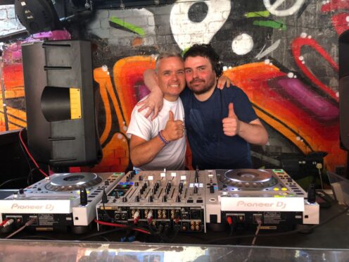 Greig Mason and Roy McLaren behind DJ decks giving thumbs up gestures