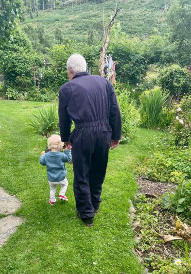 Older man in blue boiler suit walking away from camera hand in hand with toddler girl