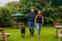 Niki Graham, Rich Burniston and Jasper, a black Lab, walking through the beer garden at the Smiddy Haugh Inn