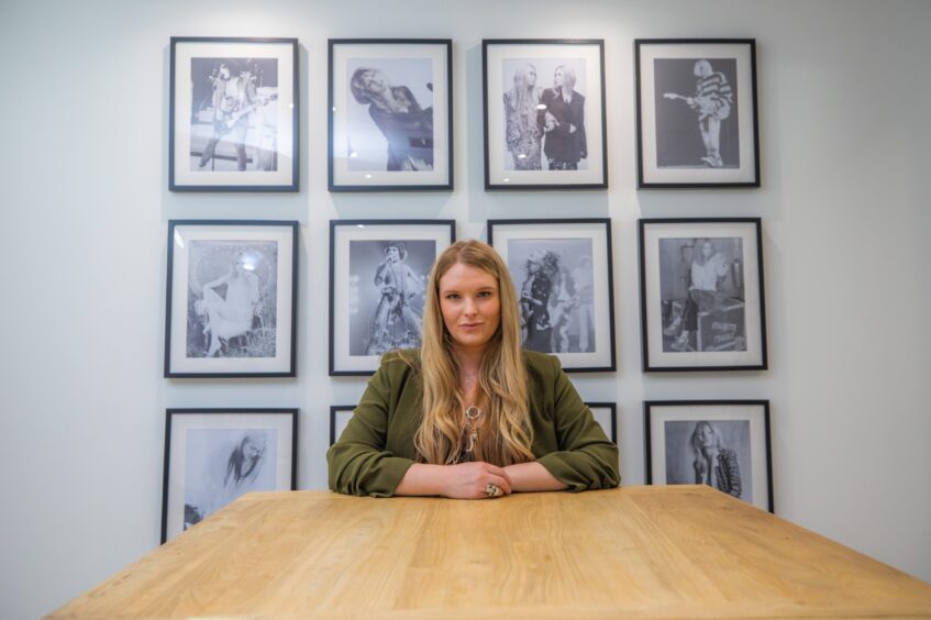 Jade Robertson seated at table with photos of music stars on the wall behind