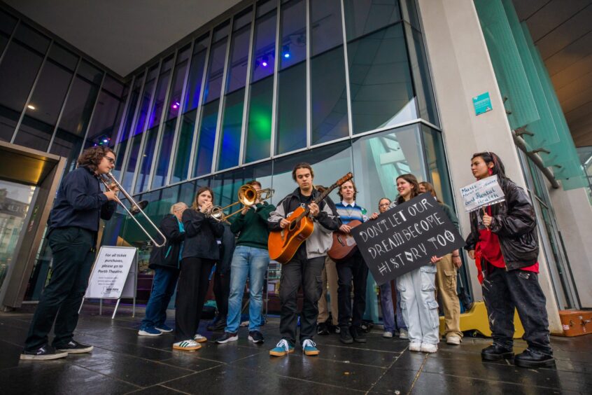 Young people playing instruments and holding placards outside Perth Concert Hall