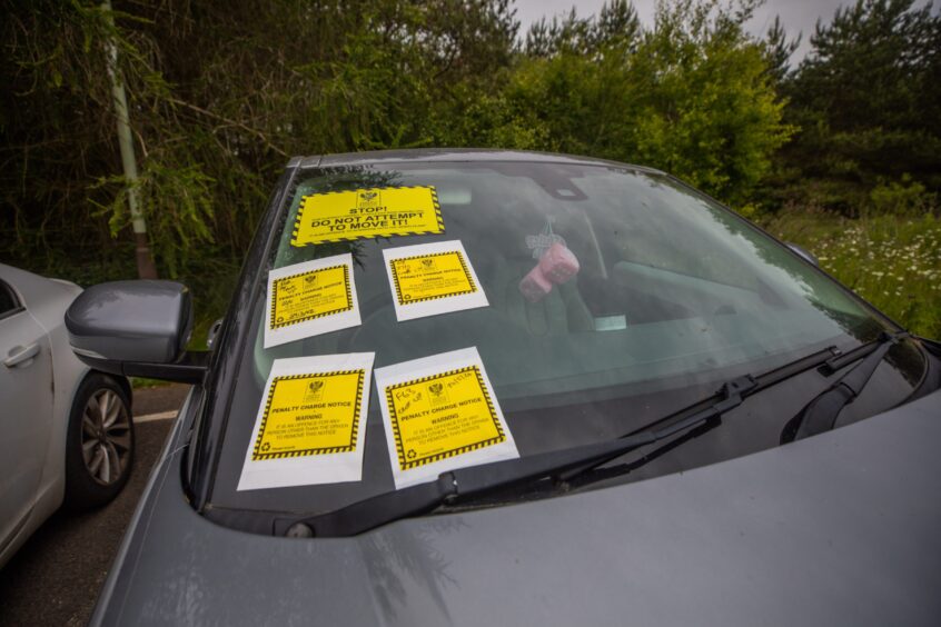 Numerous tickets on the windscreen of one car.