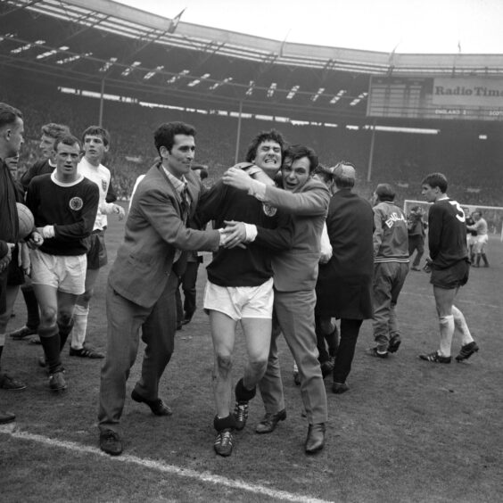 Scotland's Jim Baxter is hugged by fans on the pitch in 1967. 