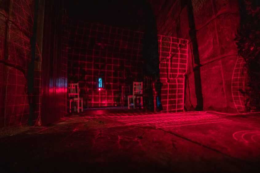 Image shows an ancient chapel at Balgonie Castle in Fife. The room is glowing red with light from a grid cast by laser which aims to detect movement from any ghosts present.