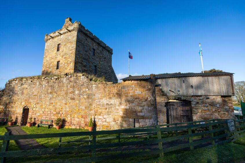 Image shows an exterior shot of Balgonie Castle in Fife on a sunny evening. The sky is blue and there is a flag flying above the castle walls.