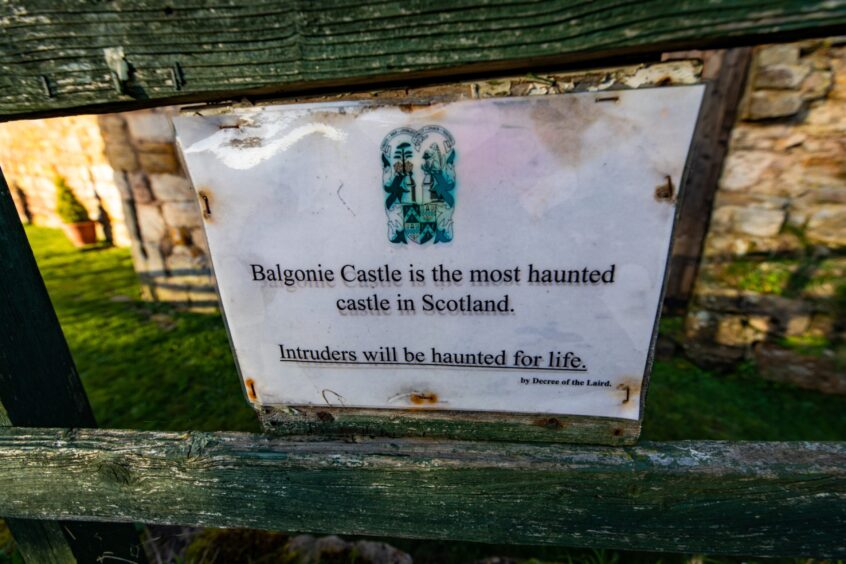 Image shows a weather-worn sign posted to a gate at Balgonie Castle in Fife. The sign reads: Balgonie Castle is the most haunted castle in Scotland. Intruders will be haunted for life!
