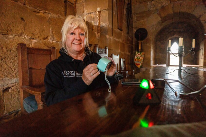 Image shows: Louise Walker setting up some of the equipment in the Great Hall at Balgonie Castle. Louise has her long blond hair tied up and is similing at the camera. She is wearing a black fleece top and is holding a device.