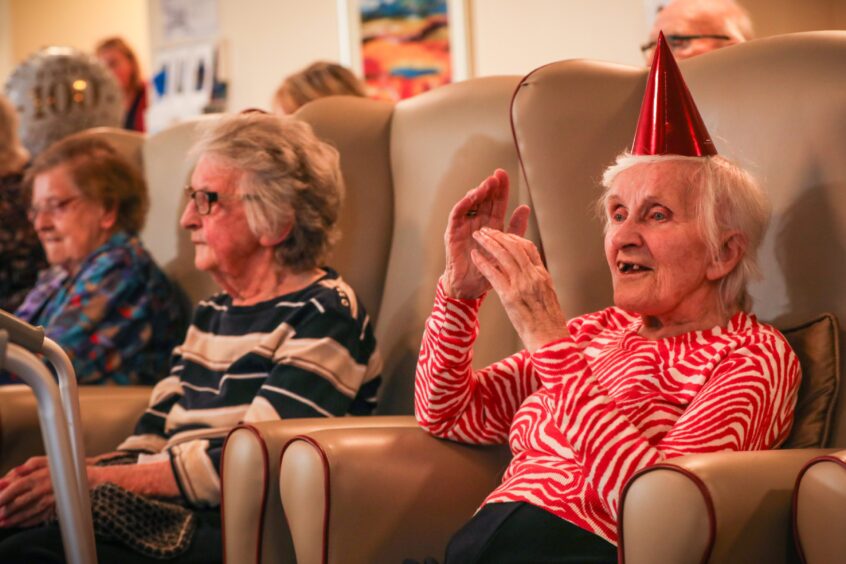 Older lady in party hat clapping along to music