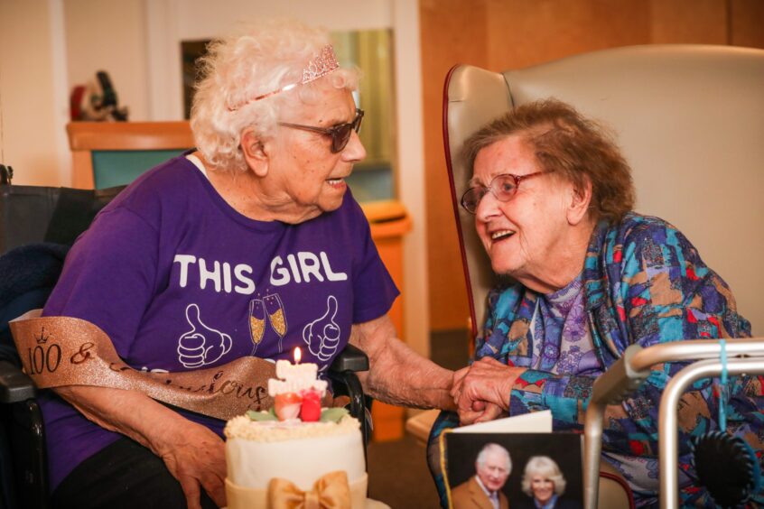 Hilda Stewart in purple t shirt and tiara speaking to another older lady during her 100th birthday party