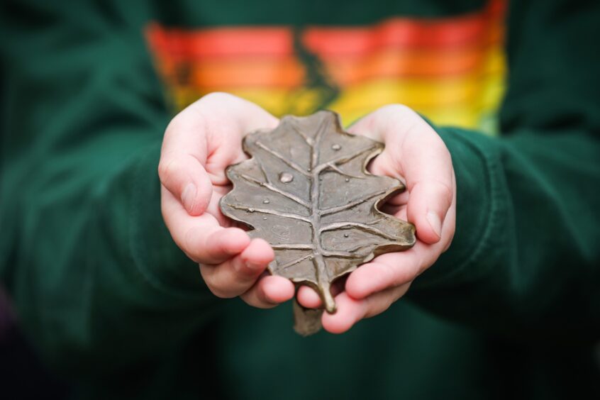 Hands holding bronze leaf sculpture