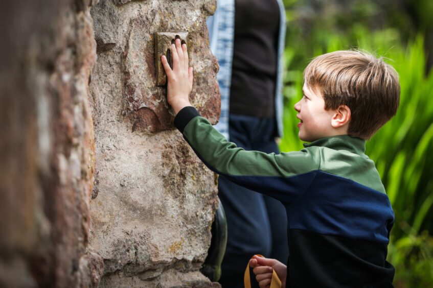 Young boy putting his hand up to touch bronze plaque on wall