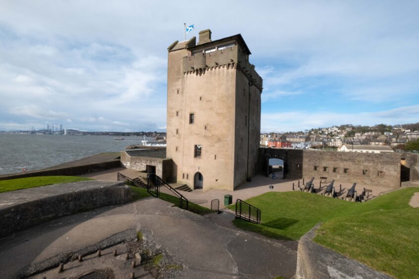 An exterior view of Broughty Castle. The imposing castle tower sits against a grey Tay Estuary and cloudy blue sky.