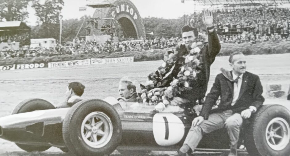 Lotus designer Colin Chapman is on the right, while Jim Clark is sitting on the car and Derek Wild is next to him, just above the steering wheel.