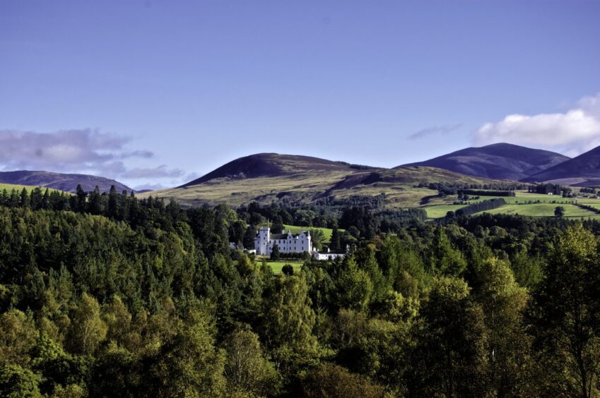 Blair Castle in Pitlochry. The white building is shown in the distance surrounded by woodland and the Perthshire hills.