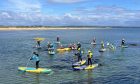 Image shows: Young people enjoying a paddleboard session at West Sands in St Andrews on a sunny summer day. There is a group of paddleboarders enjoying the watersports.