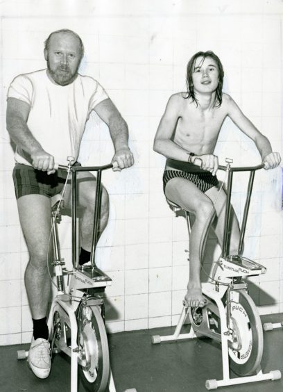 Two people ride bike machines at the swimming baths. 