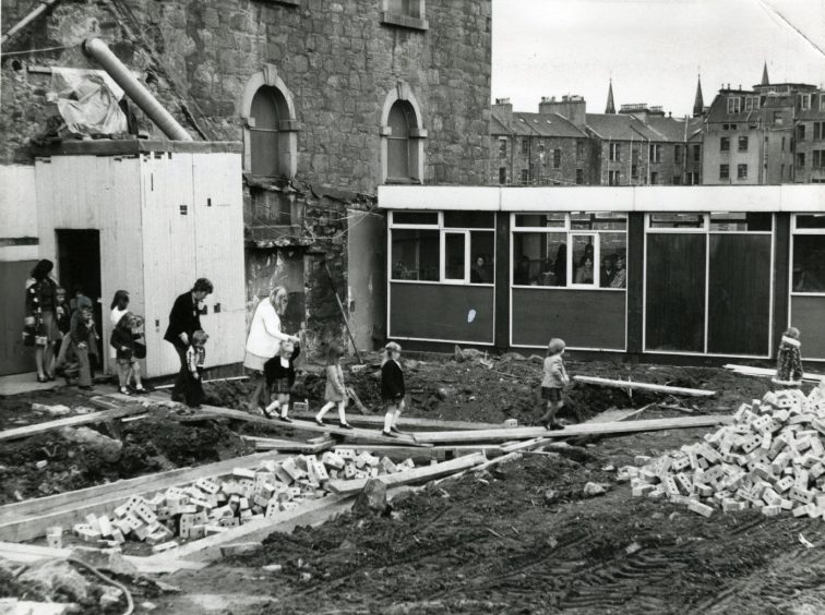 Adults and children walk on boards across rubble and dirt as rebuilding work goes on at St Andrew's Church. 