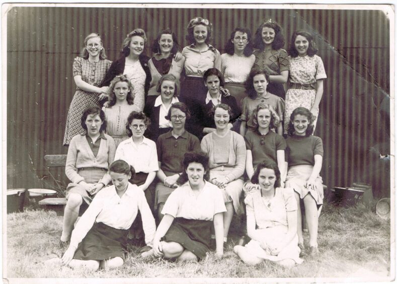 Image shows: a black and white photograph taken in 1943 of a group of Dundee schoolgirls who worked picking berries in Blairgowrie. The girls look happy and relaxed as they pose together with two teachers from Harris Academy.