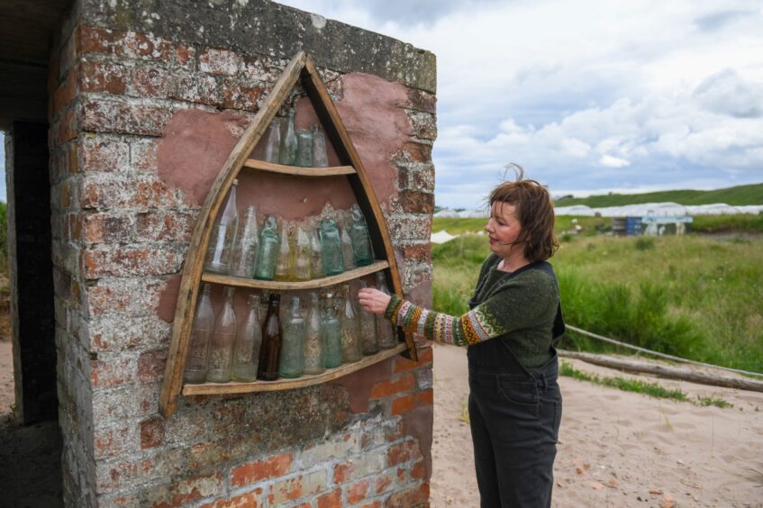 Jillian McEwan with some of the vintage glass bottles collected on the beach and now decorating the lookout pillbox at Lunan Bay Farm. Image: Kim Cessford. 