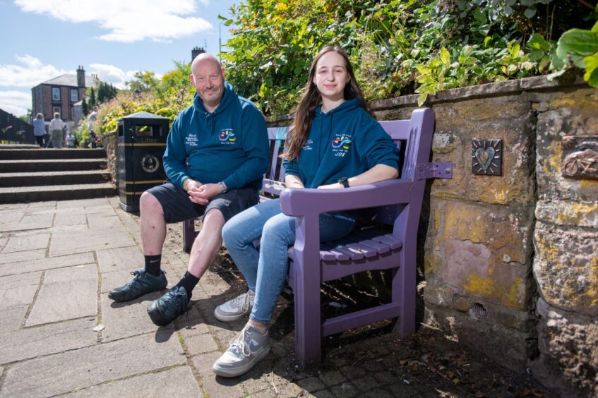 Gavin Hart and Joselyn Turner smiling, seated on purple wooden bench in sunshine