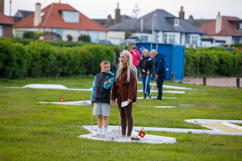 Image shows: a mother and son playing crazy golf on the mini golf course at West Braes in Pittenweem. The traditional style mini golf course has painted holes with obstacles for players to avoid.