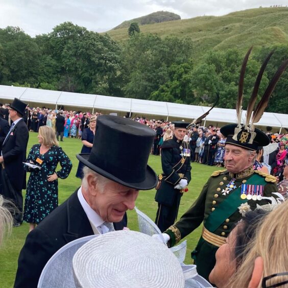 King CXharles in top hat laughing with group of women at royal garden party in Edinburgh