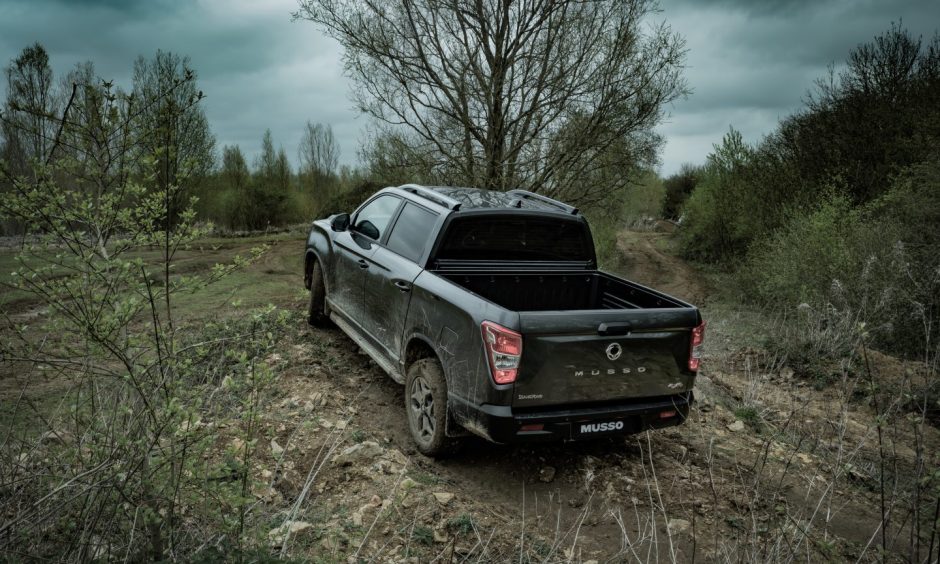 the KGM Musso seen from behind in a muddy field