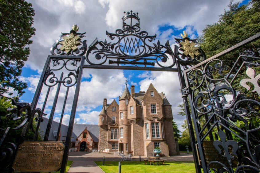 The exterior of the Black Watch Castle and Museum in Perth. The castle is viewed through a wrought iron gate against the backdrop of a cloudy blue sky. 