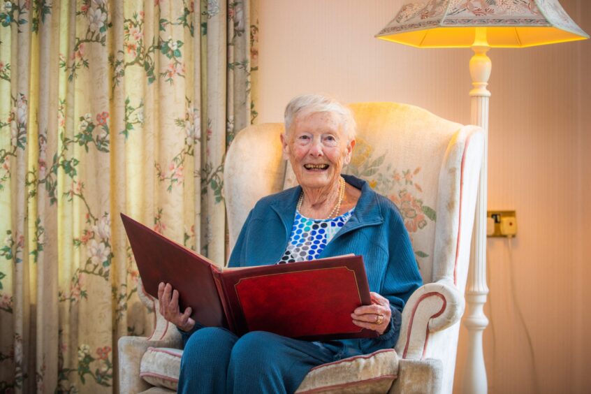 Image shows: Dorothy Christie, age 96, in an armchair at her home in Auchterarder. Dorothy is smiling widely at the camera and is holding a photo album with pictures of her with her school friends.Dorothy had a summer job picking berries in Blairgowrie in 1943.