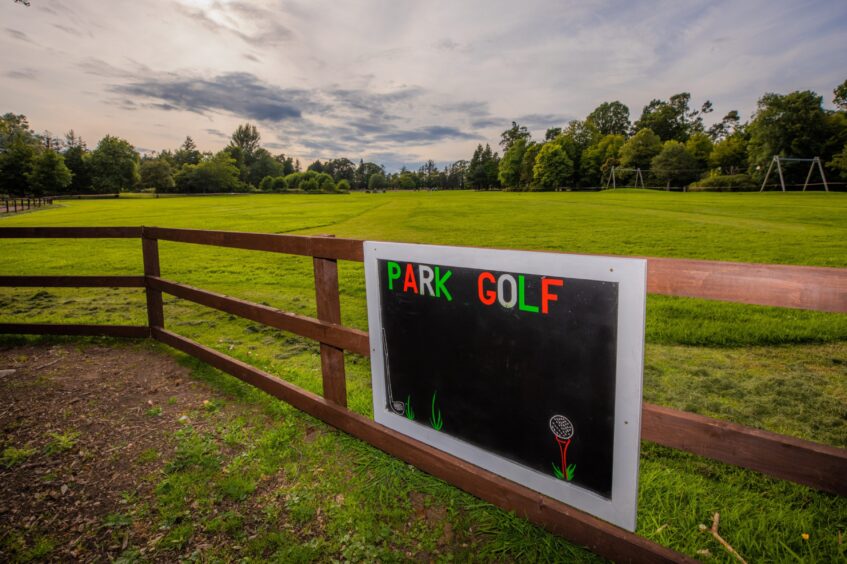 Image shows: The Park Golf course at Craigtoun Country Park, Fife. There is a colourful sign that says Park Golf with the grassy course in the background of the image against a blue cloudy sky.