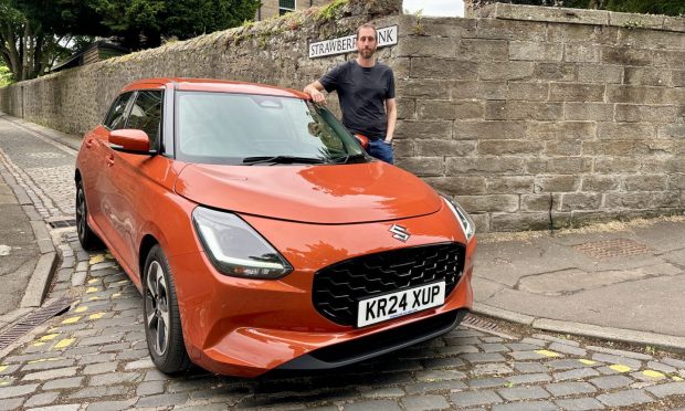 Jack McKeown stands beside an orange Suzuki Swift parked on a cobbled city street