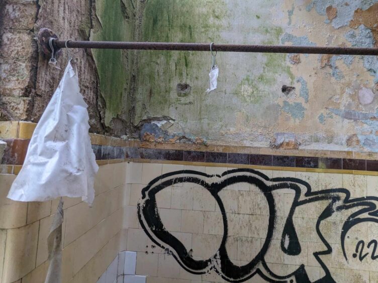 An old shower curtain hangs from a rail in abandoned Thornton Fever Hospital. Image: Gayle Ritchie.