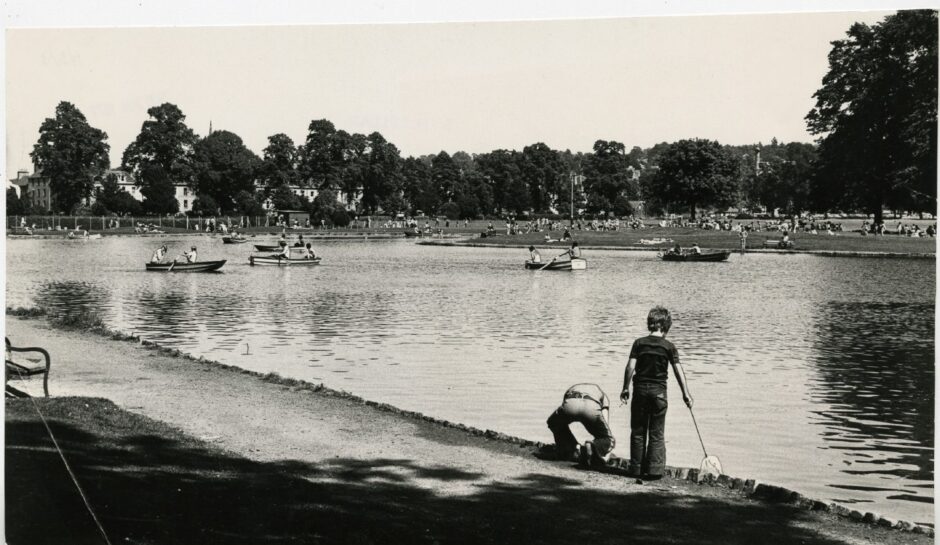 Black and white photo of South Inch pond with boats on water and children playing by the side