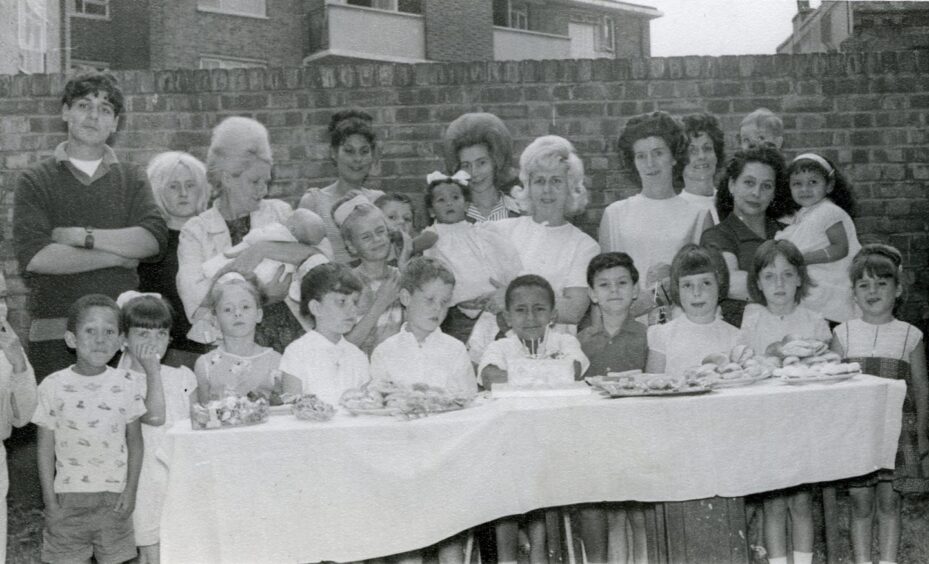 Lydia standing behind Thompson at his sixth birthday party, as mums and kids gather around an outdoor table