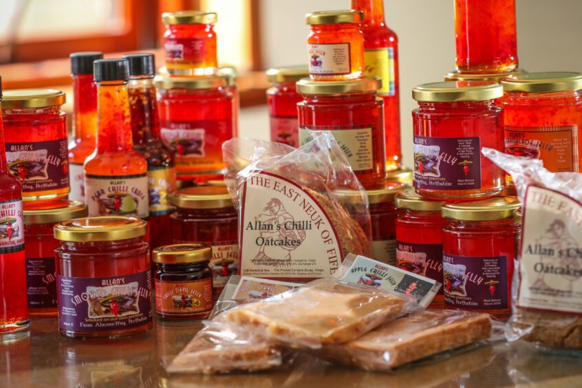 A range of Allan's Chilli Products, including bottles of chilli sauce, various sizes of chilli jellies, and packets of chilli oatcakes and chilli tablet. 