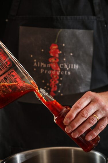 A red chilli sauce is poured into a bottle. 