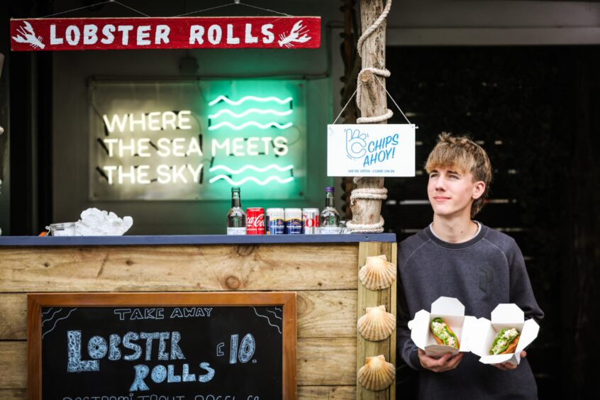 Francisco Martins stands to the right of the St Andrews seafood shack, holding two lobster rolls. 