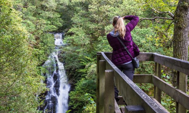 Woman photographing the Black Spout Waterfall near Pitlochry.