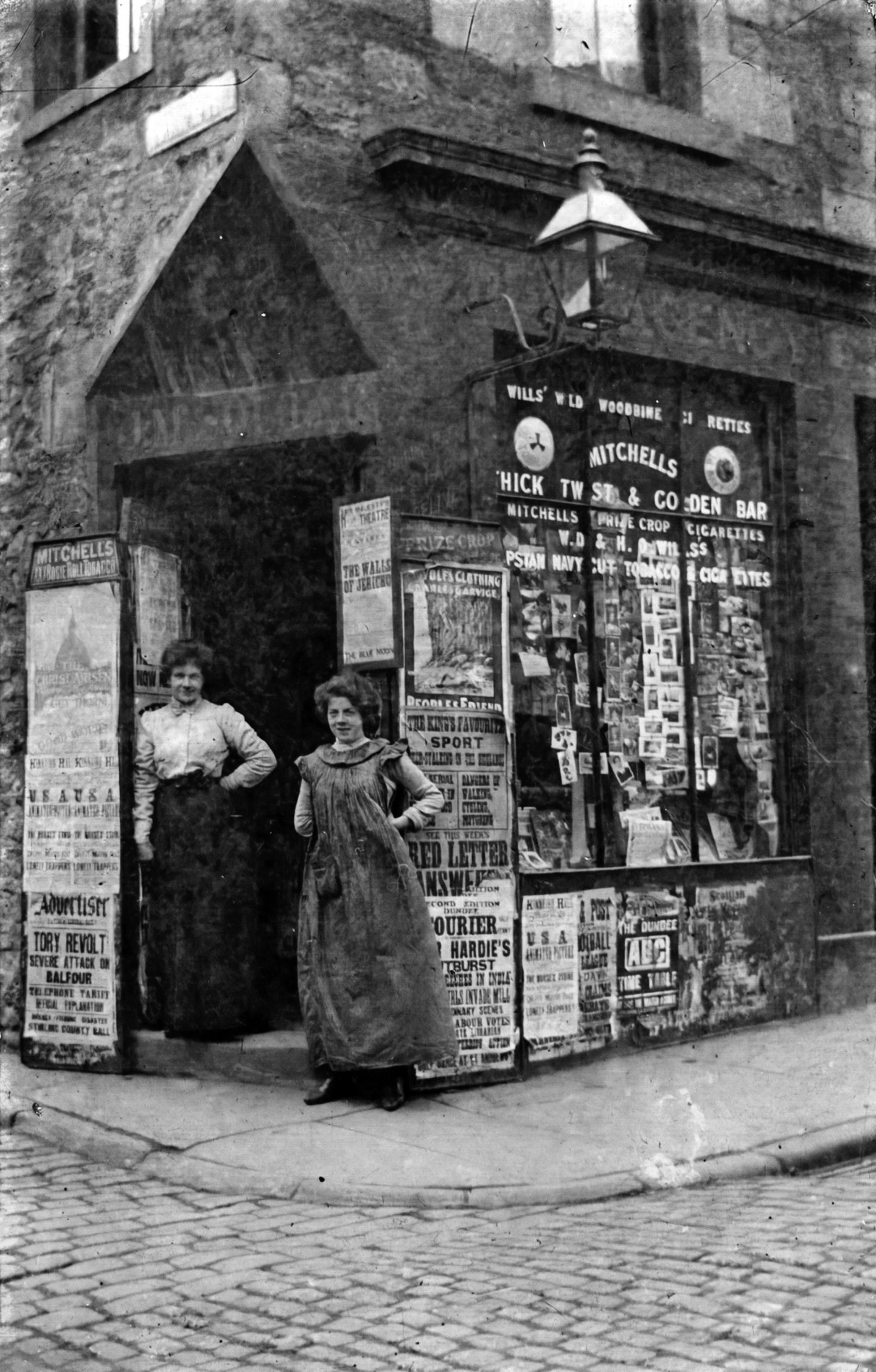 Two women pose for a picture outside a shop. The posters show the political unrest of the time.