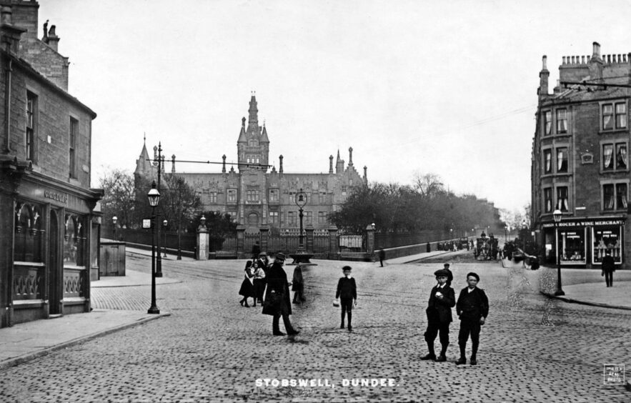 This image fro Bygone Dundee shows people crossing a street in Stobswell, with Morgan Academy in the background.