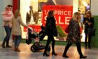 Crowds walking past shop window with sales posters in St John's shopping centre