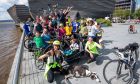 A group of around 30 cyclists posing in front of the V&A Dundee.