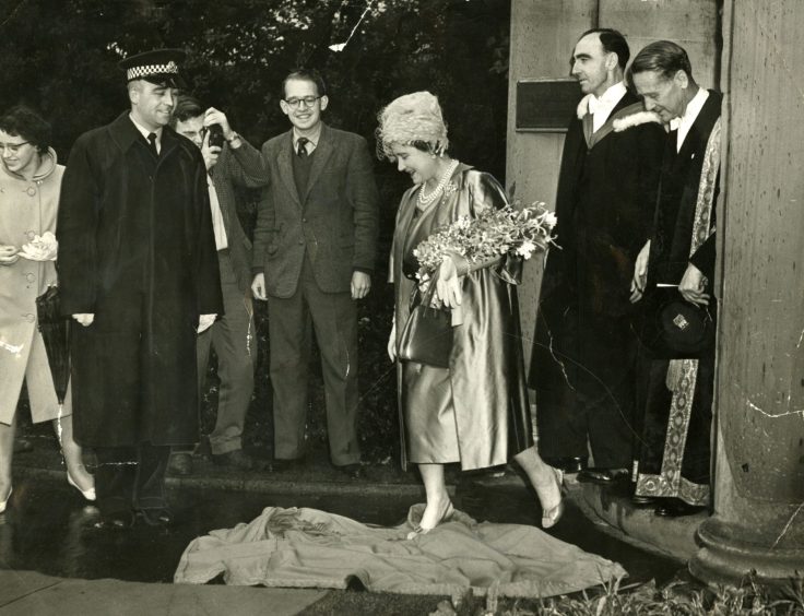 Officials look on as The Queen Mother steps on a cloak belonging to student Mike Steadman.