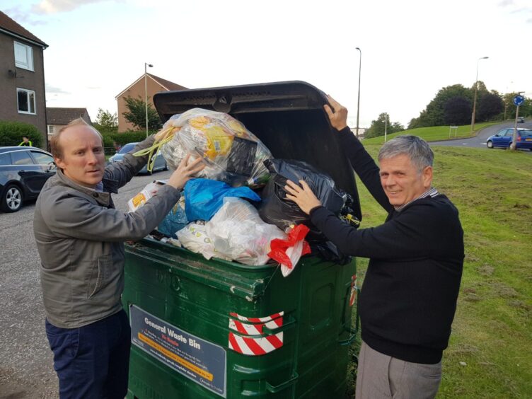 Councillor Michael Marra and Charlie Malone hard at work in Lochee, putting bags of rubbish into a skip.