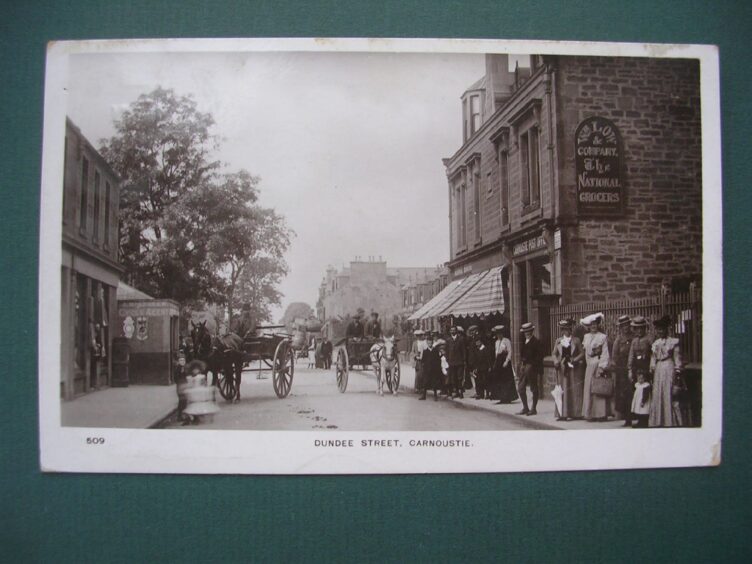 A postcard from 1907 showing a William Low shop in Carnoustie with people on the pavement and horsedrawn carriages in the street