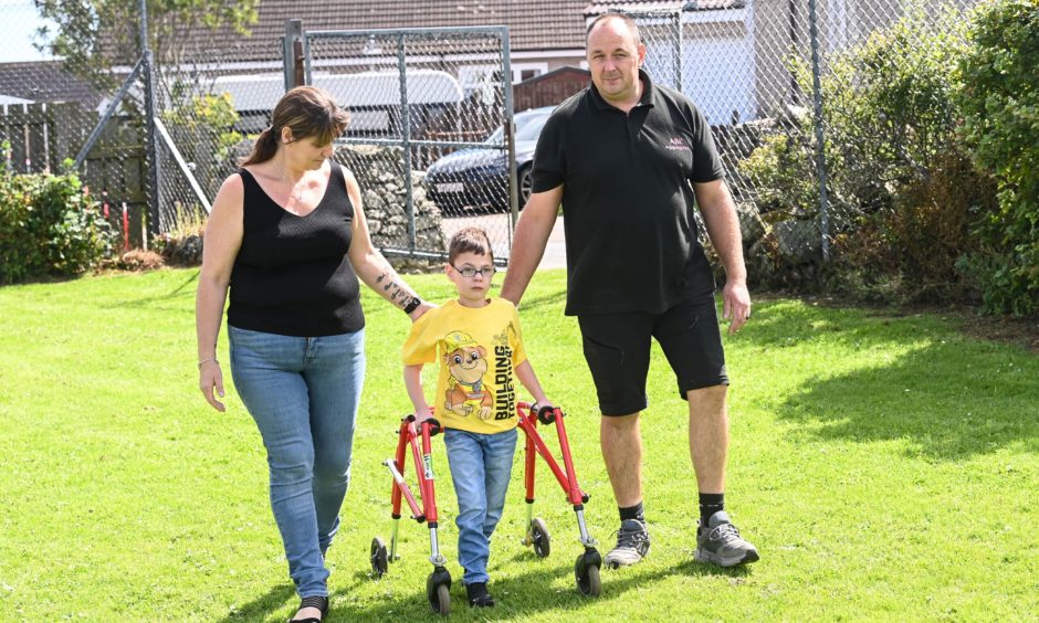 Harrison using his walking frame, with his mum and dad.